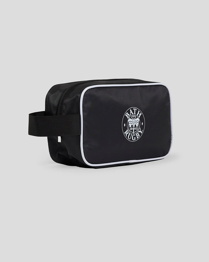 Angled side view of black Bath Rugby washbag with white piping, strap handle and front zip pocket with gold pull.