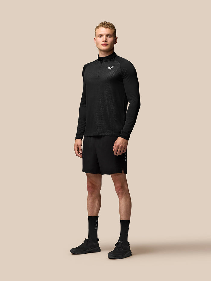 Male model in black Adapt training outfit with a long sleeve top and 6 inch stretch shorts on a beige background