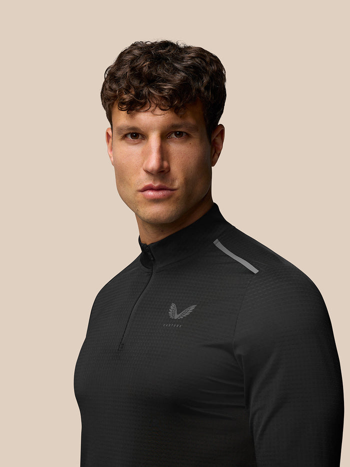 Three quarter side view of a man in black Apex Training Top with Castore logo on the chest and a reflective shoulder stripe.
