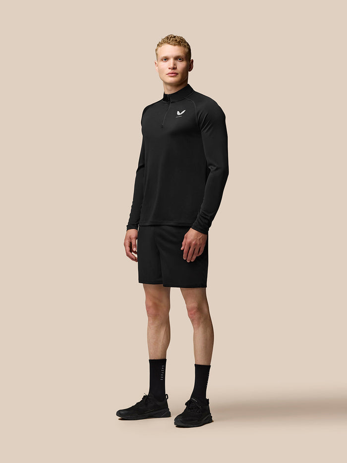 Full body shot of man in black Adapt Training Quarter Zip Top with stand collar and black shorts