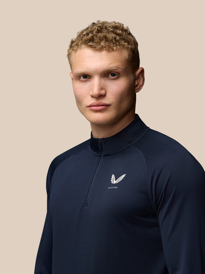 Male model wearing midnight navy Adapt Training Quarter Zip Top with stand collar and front zip, Castore logo on left chest.