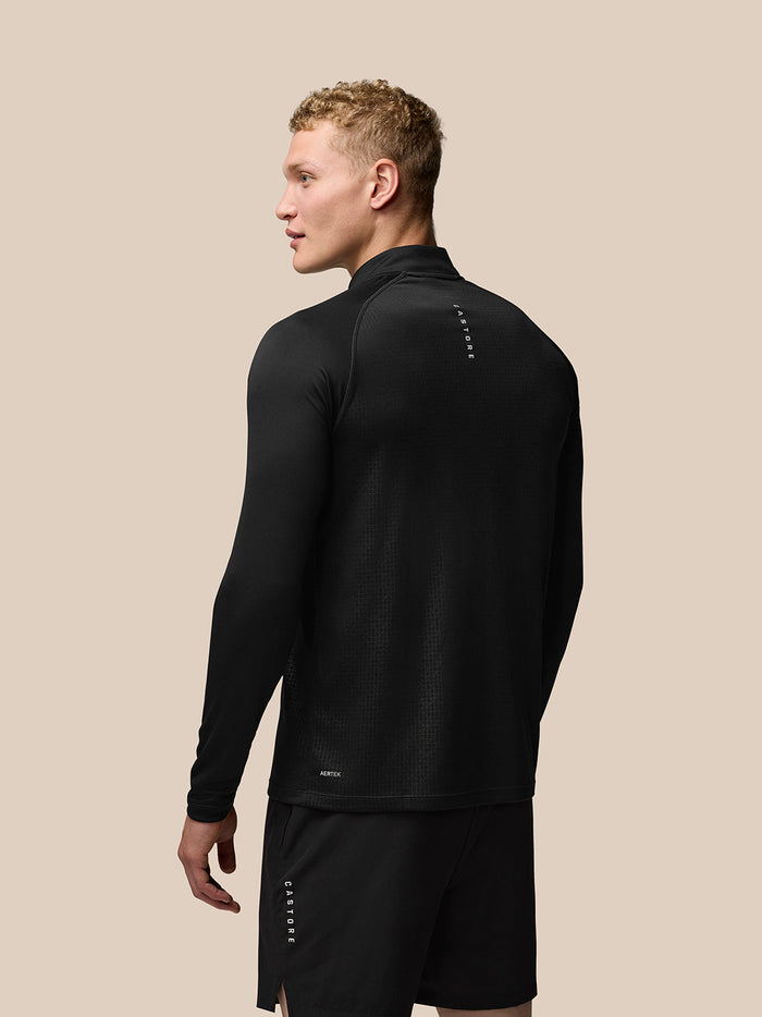 Back view of a man wearing black Adapt Print Quarter Zip Top with geometric texture and branding along the upper back and lower hem