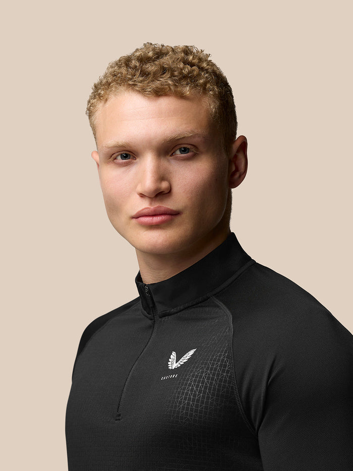 Back and side view of man in black Adapt Print Quarter Zip Top with Castore logo on left chest and upper back and Aertek branding at the lower back