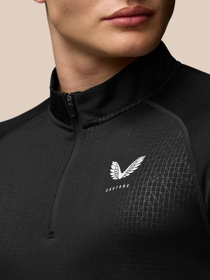 Close up of black Adapt Print Quarter Zip Top showing stand collar, quarter zip and wing Castore logo on left chest with a subtle geometric grid pattern