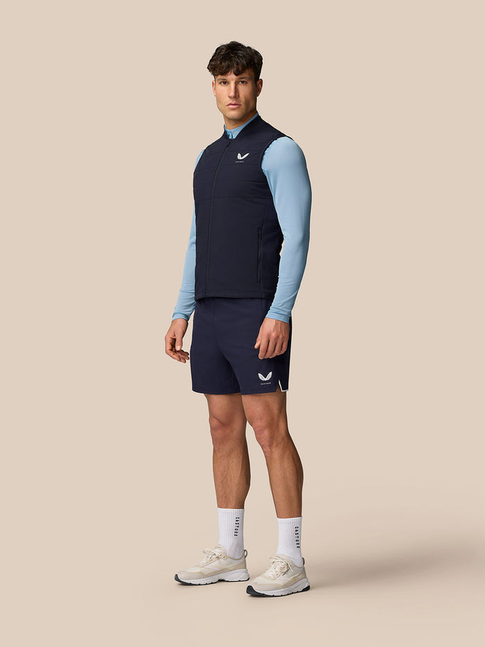 Male model wearing navy Apex Training Gilet over a light blue long sleeve top with navy shorts