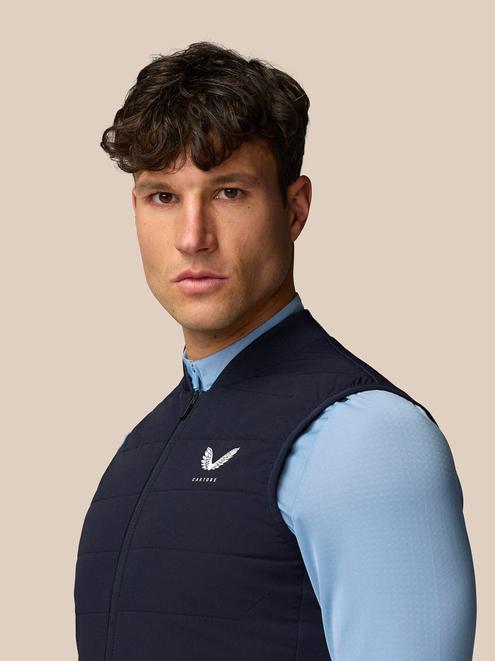 Male model wearing navy quilted gilet over a light blue shirt with Castore logo on the chest.