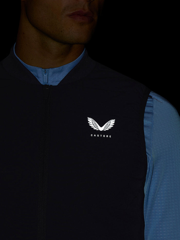 Close-up of the gilet chest with zipper and Castore logo, blue sleeve detail visible.