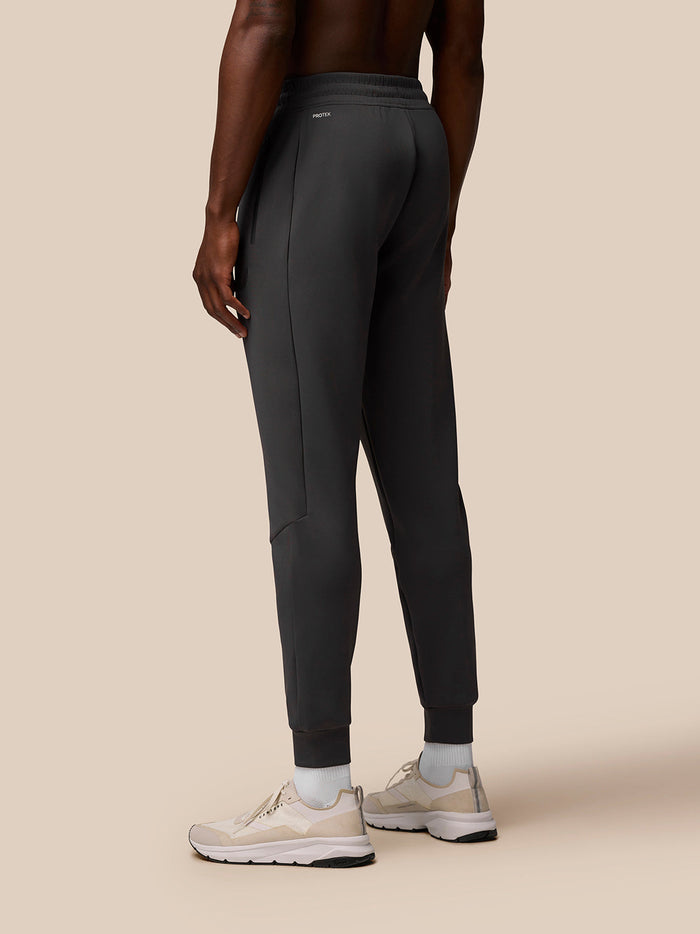 Back view of a man wearing charcoal Flex Lifestyle Joggers with branded left thigh and rear logos.