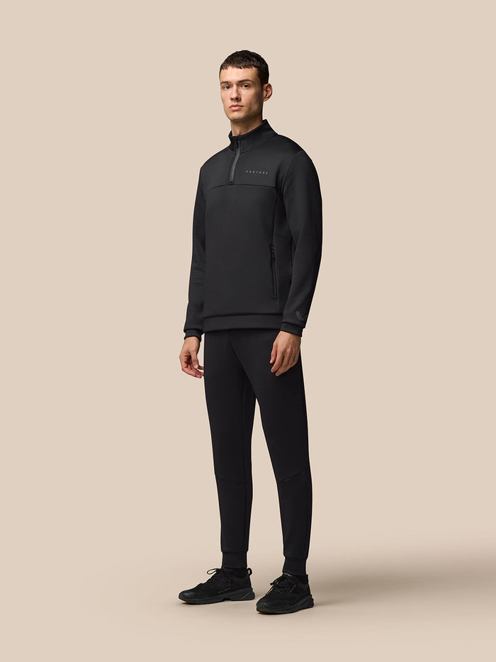 Full-body shot of a man in black Flex Lifestyle Joggers with a matching top against a beige background