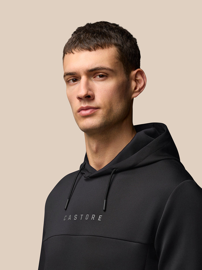 Male model wearing black Flex Hoodie with hood and drawstrings, Castore branding on chest.