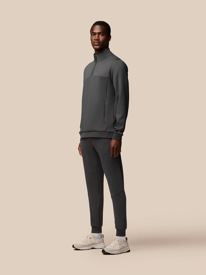 Male model wearing charcoal Flex Quarter Zip top with zip pockets and Castore branding, paired with matching joggers.