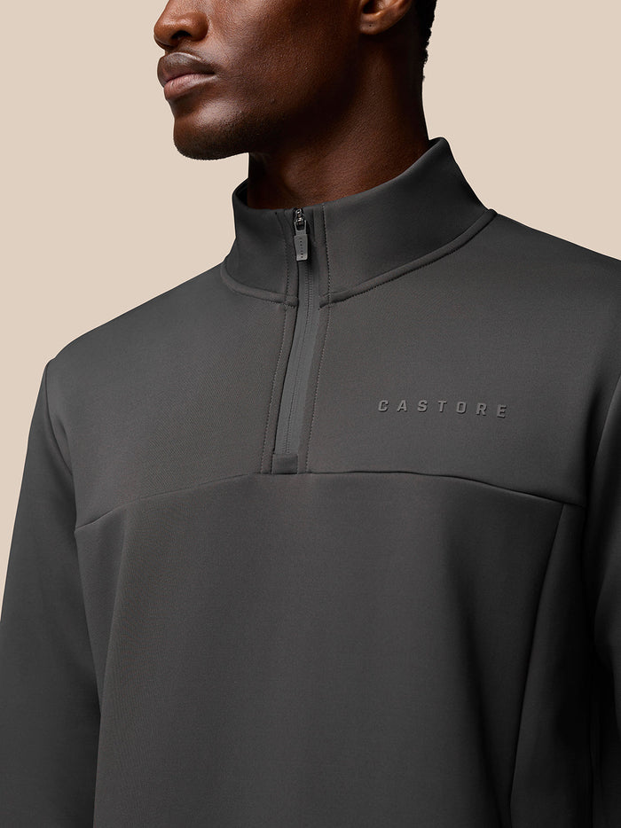 Close-up of charcoal Flex Quarter Zip top showing high collar, front zipper and Castore branding on the left chest.