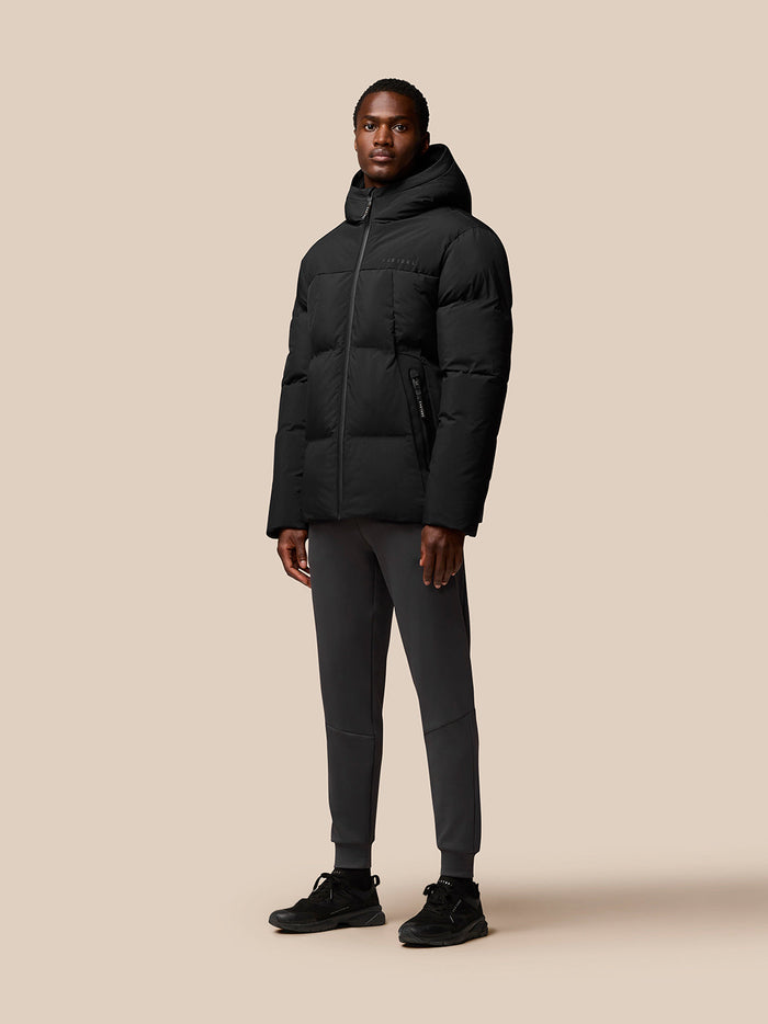 Male model wearing a black hooded puffer jacket with front zipper and zip pockets