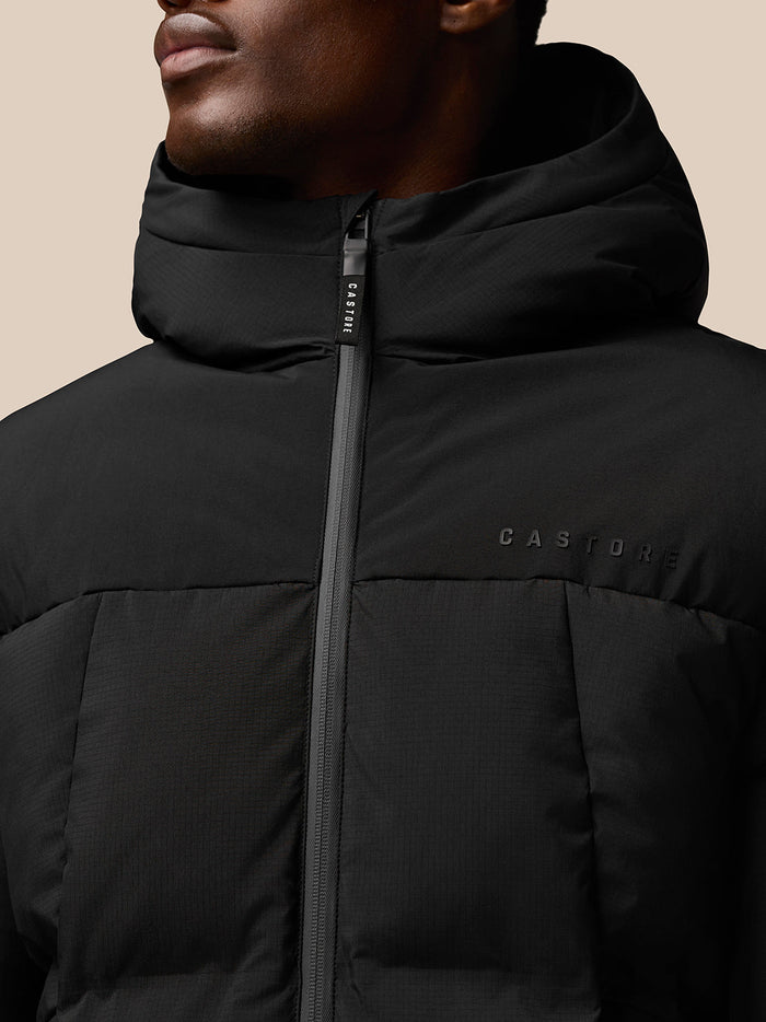 Close-up of black puffer jacket showing center front zip, hood and Castore branding on chest with ProTek branding on sleeve