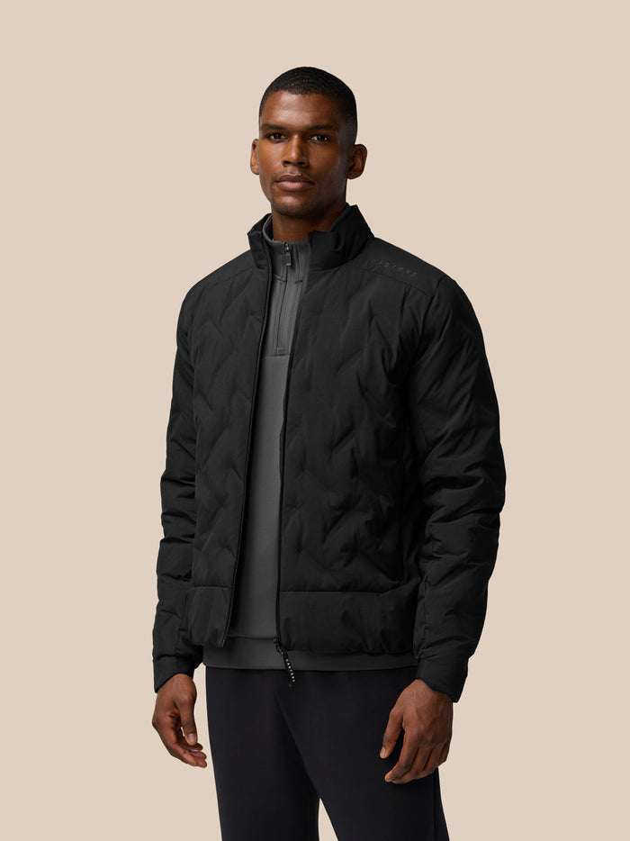 Male model in black padded jacket with high collar and zip front against a beige background.
