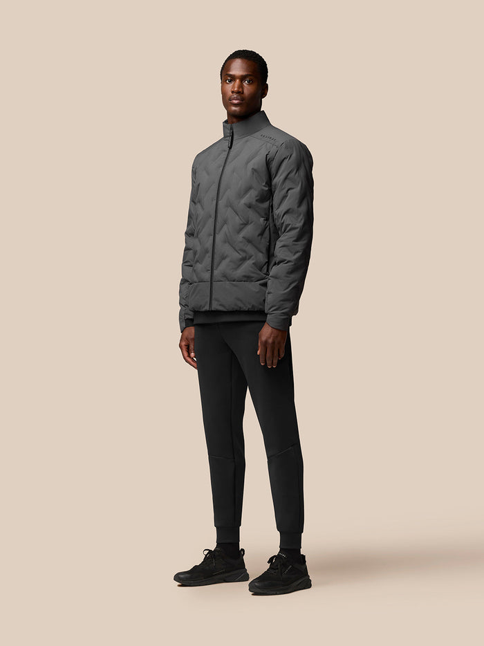 Model wearing charcoal Quilts Lifestyle Jacket front view with full zip and stand collar, paired with black joggers.