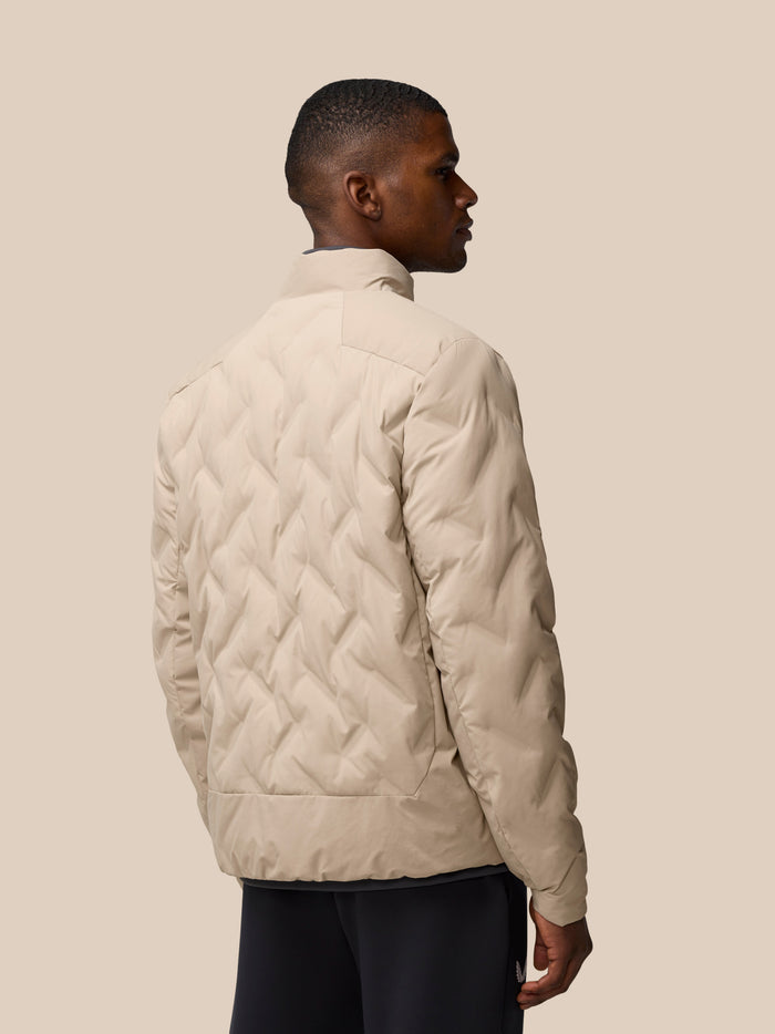 Side profile of a man in a beige padded jacket, showing the quilted back and relaxed pose.