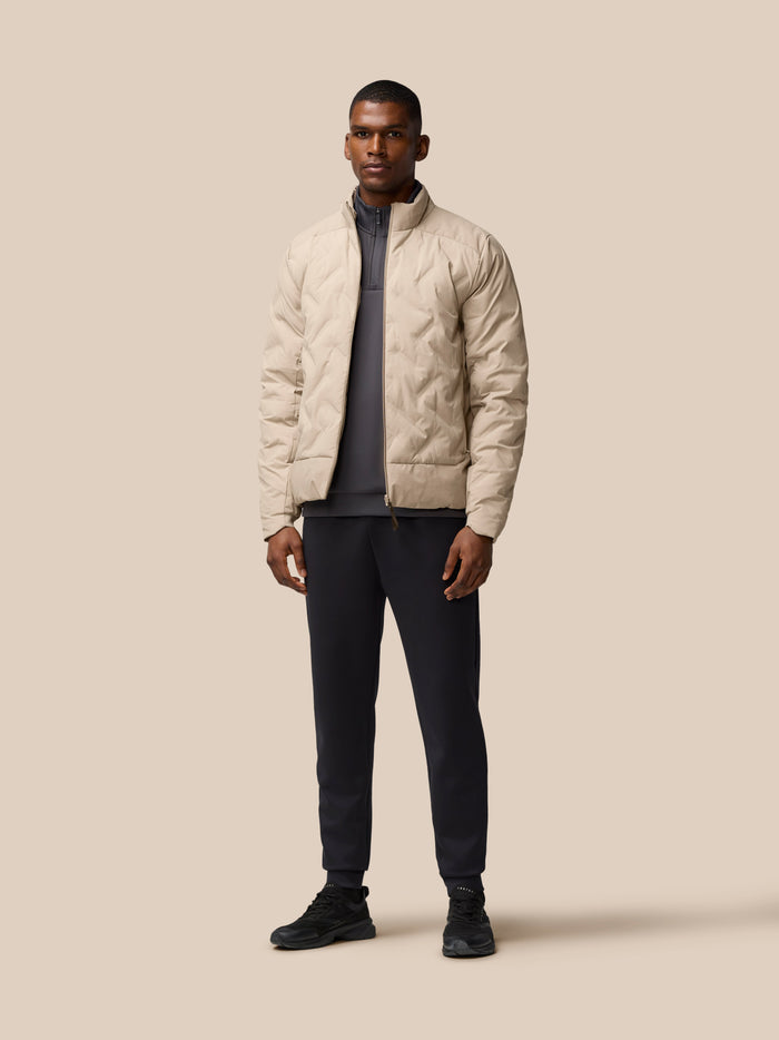 Male model wearing a beige padded jacket with zip front and high collar against a neutral background.