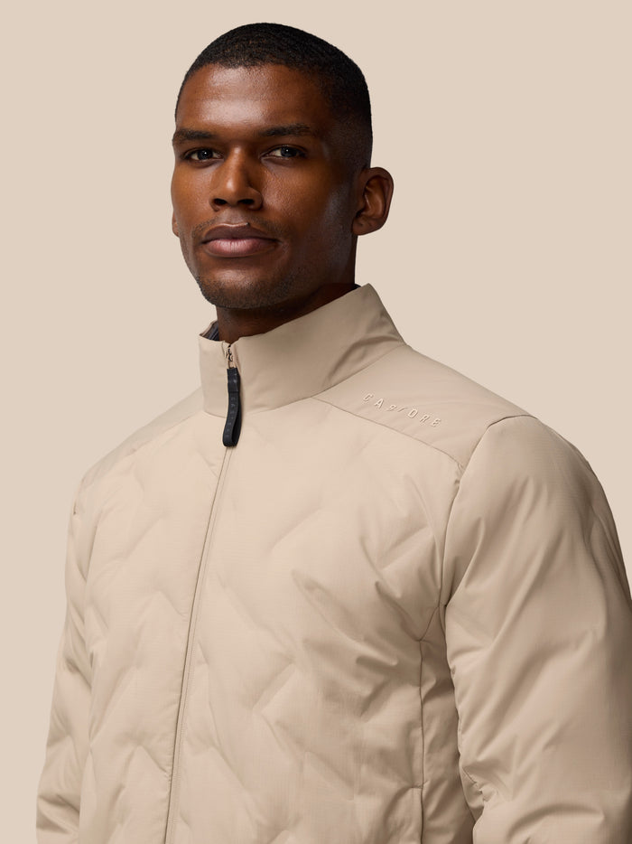 Close-up of a man in a beige padded jacket with stand collar, front zipper, Castore branding visible.