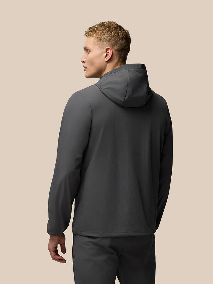 Back view of a man wearing a dark charcoal Flex Classic Set Woven Jacket with hood