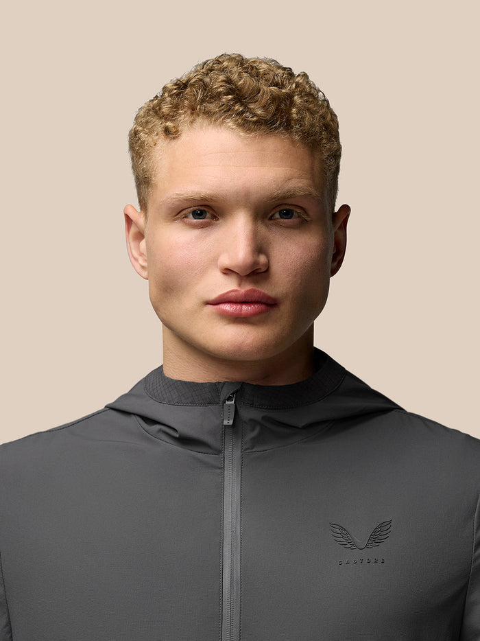 Close-up portrait of a male model wearing a charcoal zip-up jacket with a small left chest logo.