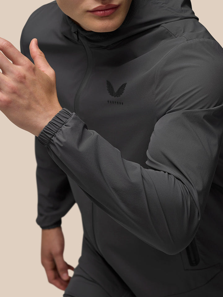 Close-up of a model wearing a charcoal lightweight Flex Jacket with hood and left chest branding.