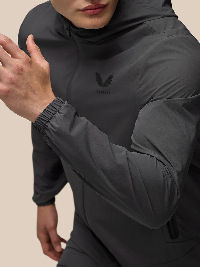 Close-up of a model wearing a charcoal lightweight Flex Jacket with hood and left chest branding.