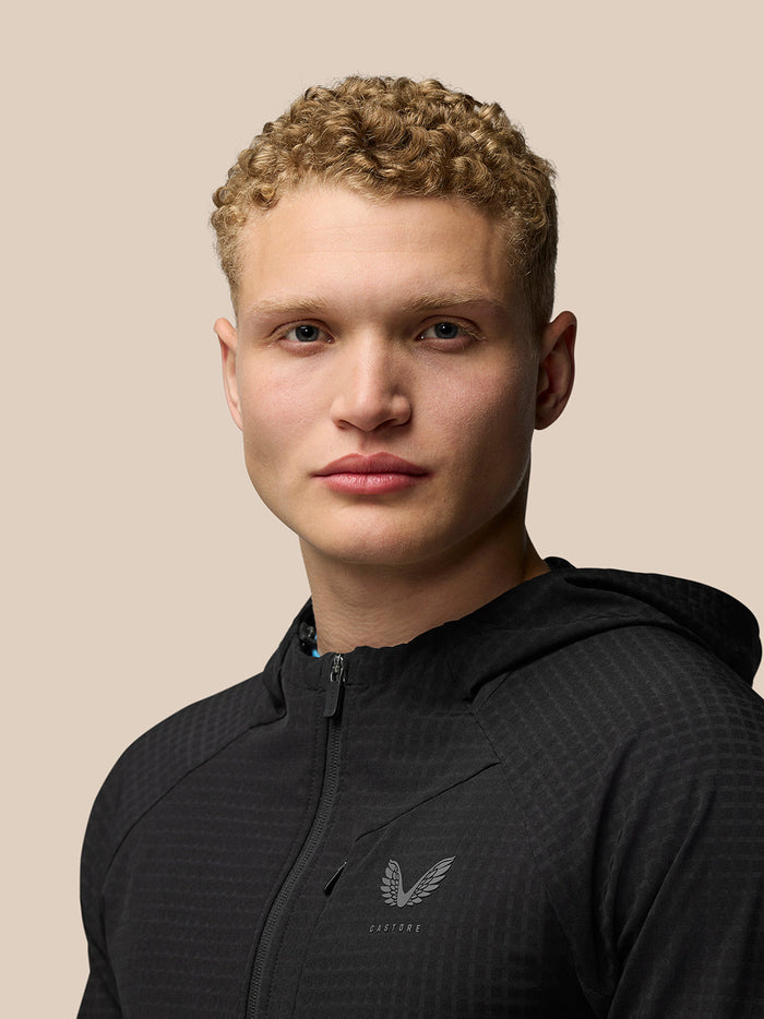 Three-quarter view of a male model in black Flex Winterised Jacket with hood down and chest logo.