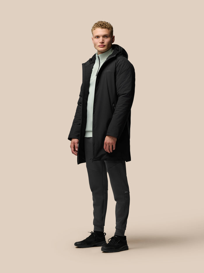 Male model wearing black longline wadded jacket with hood, centre front zip and external pockets