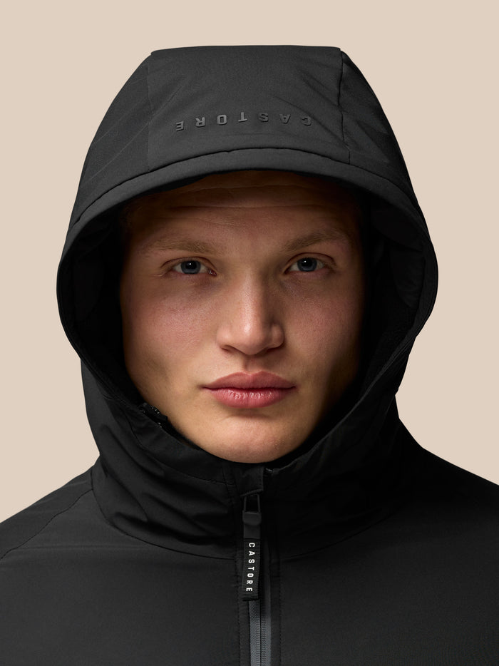 Close up of a model wearing a black longline wadded ProTek jacket with hood up and CASTORE branding on the zipper.