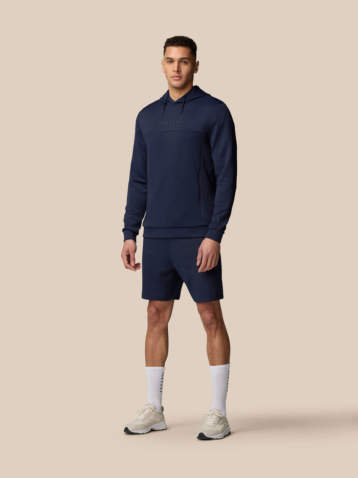 Male model wearing navy Flex Lifestyle shorts with matching hoodie against a beige background