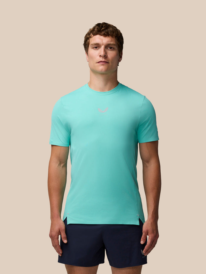 Male model in light aqua Zone Training T Shirt with chest logo and navy shorts on a beige backdrop