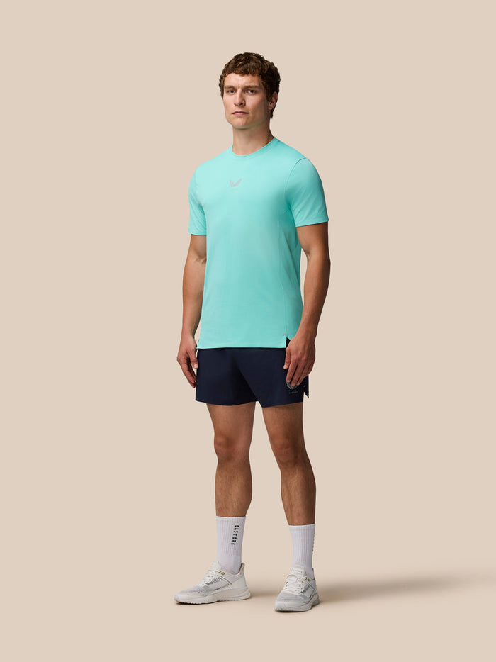 Full body shot of a man in a light aqua Zone Training T-Shirt with navy shorts against a beige backdrop.