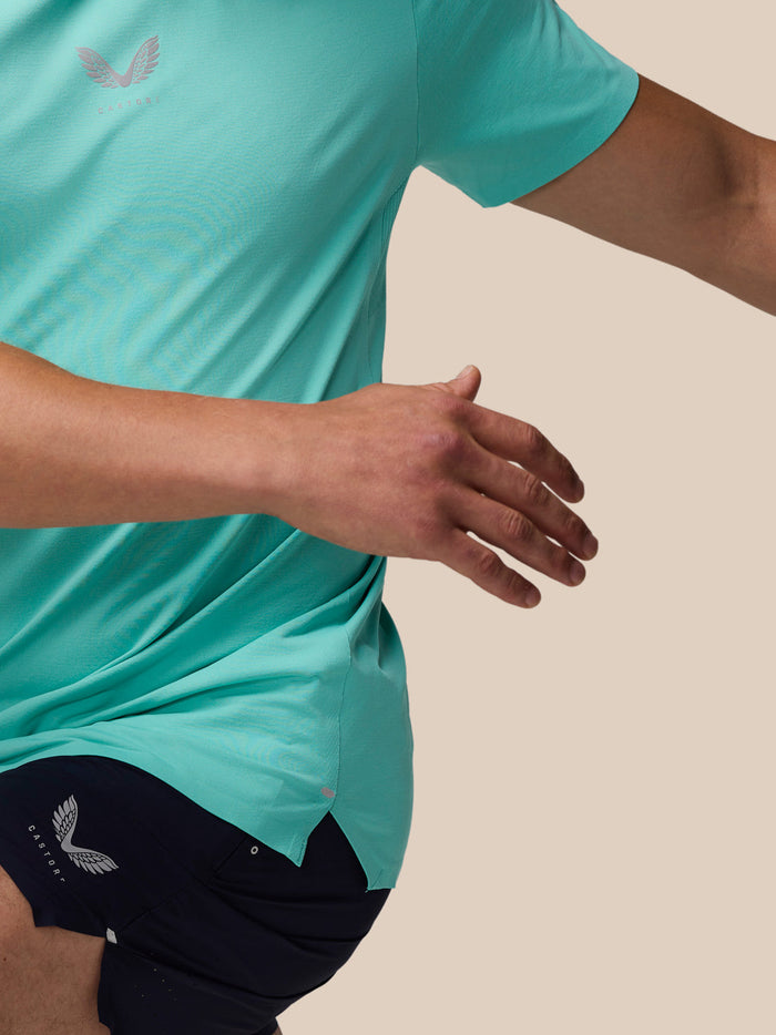 Side view of a man in a light aqua Zone Training T-Shirt and navy shorts with a logo on the shorts near the hem.