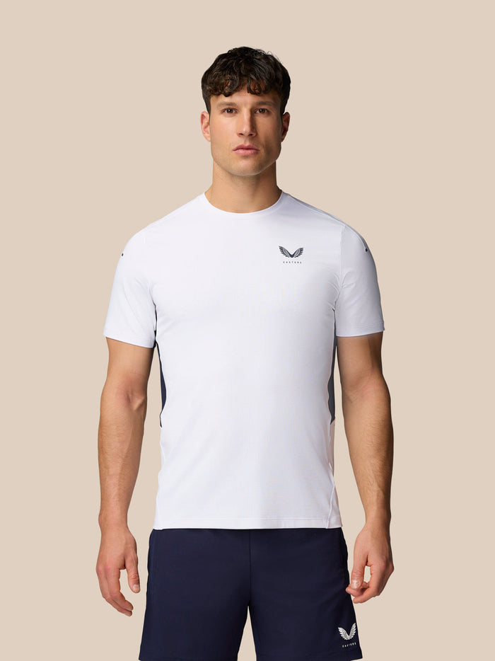 Male model wearing white Apex Training T-Shirt with Castore logo on chest and navy shorts.