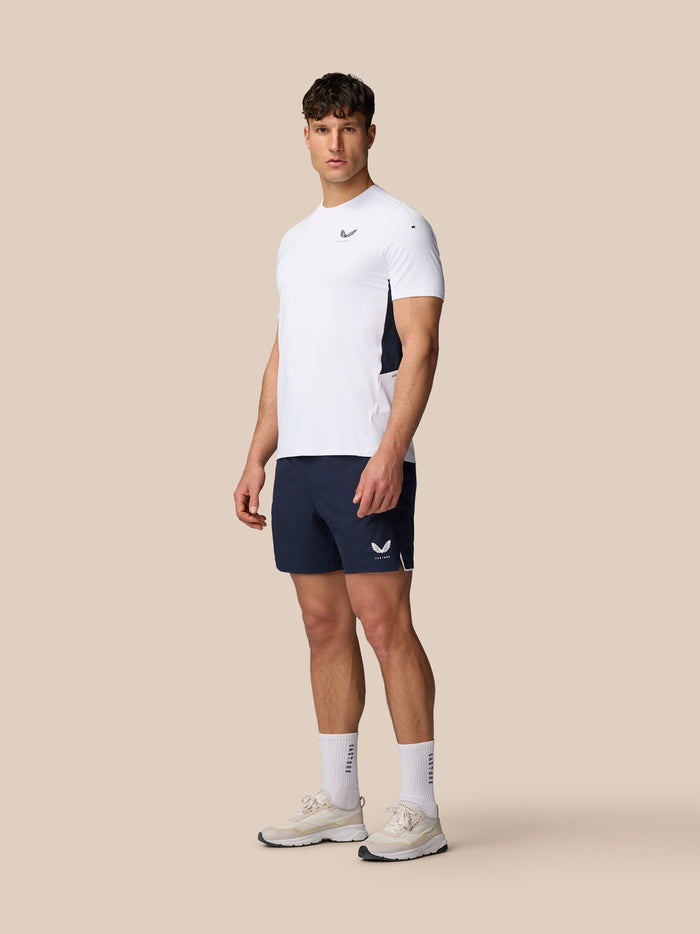 Full-body side view of male model in white Apex Training T-Shirt with navy shorts.