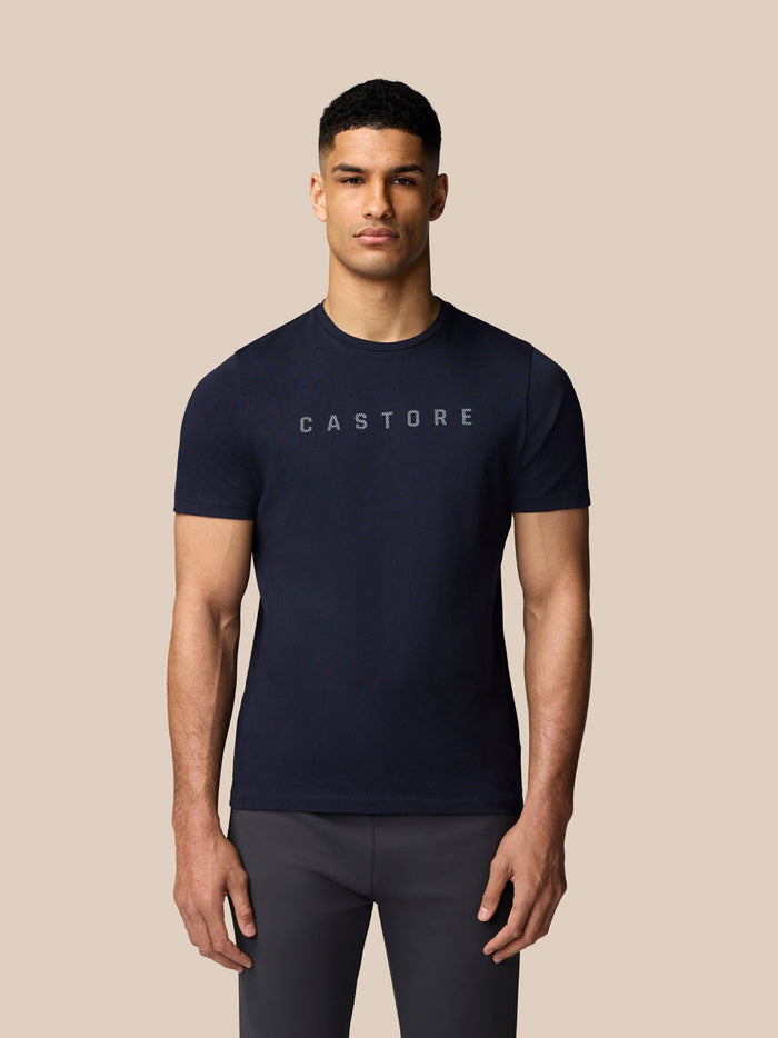 Male model wearing navy Graphic Lifestyle T-Shirt with Castore logo across the chest against a beige backdrop.