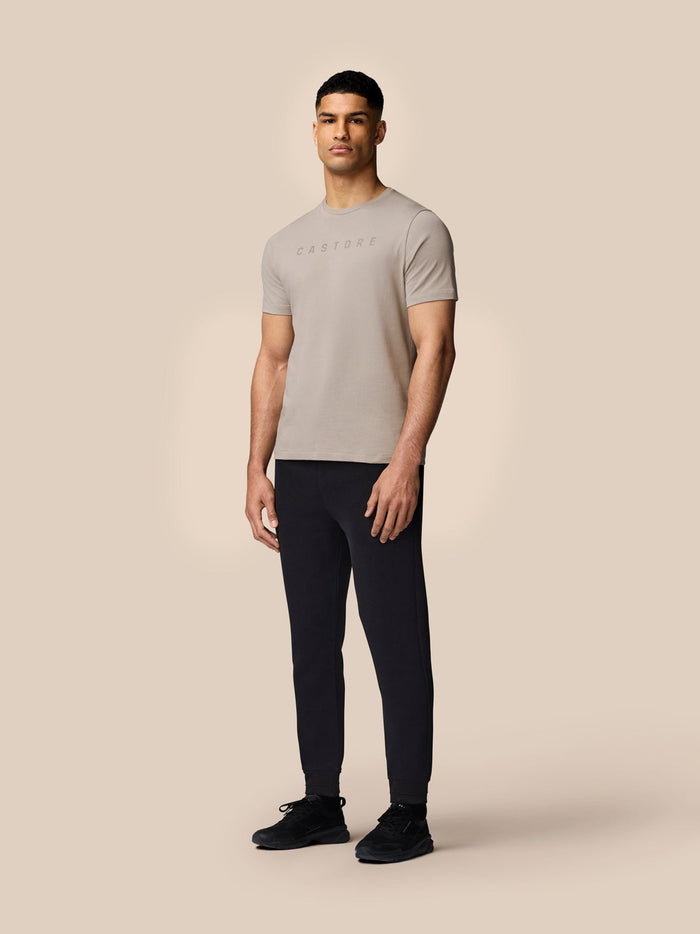 Full-body view of a man in a Rock Grey Castore graphic T-shirt with dark joggers against a neutral backdrop