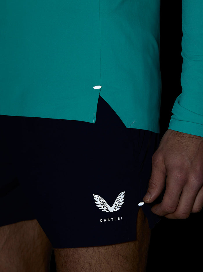 Close-up of Zone Training 1/4 Zip Top in light aqua showing teal knit fabric and bonded hem detail with navy shorts.