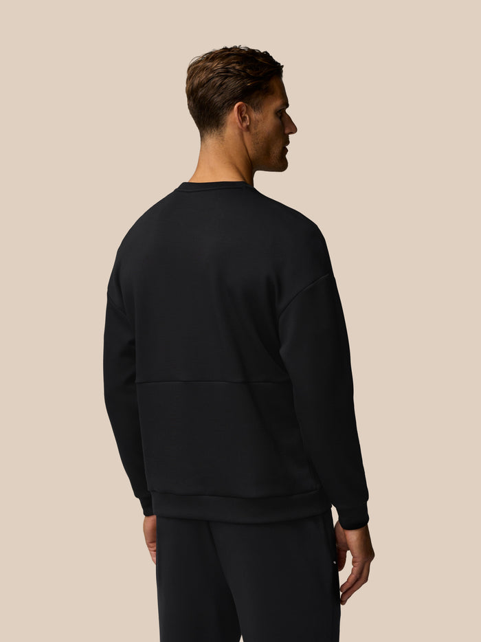 Back view of a man wearing a black Travel Lifestyle Sweatshirt against a beige background