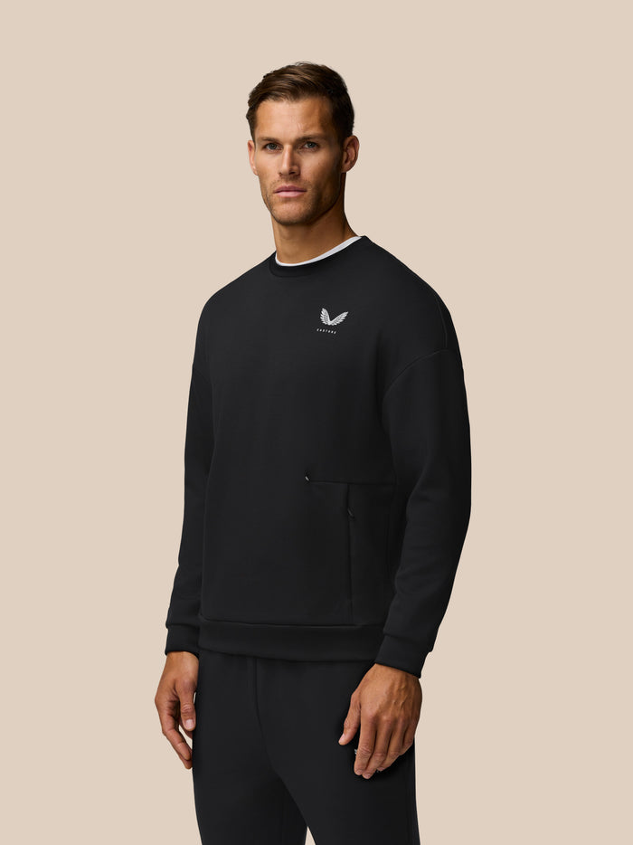 Male model wearing black Travel Lifestyle Sweatshirt with white wing logo and a zip pocket against a beige background