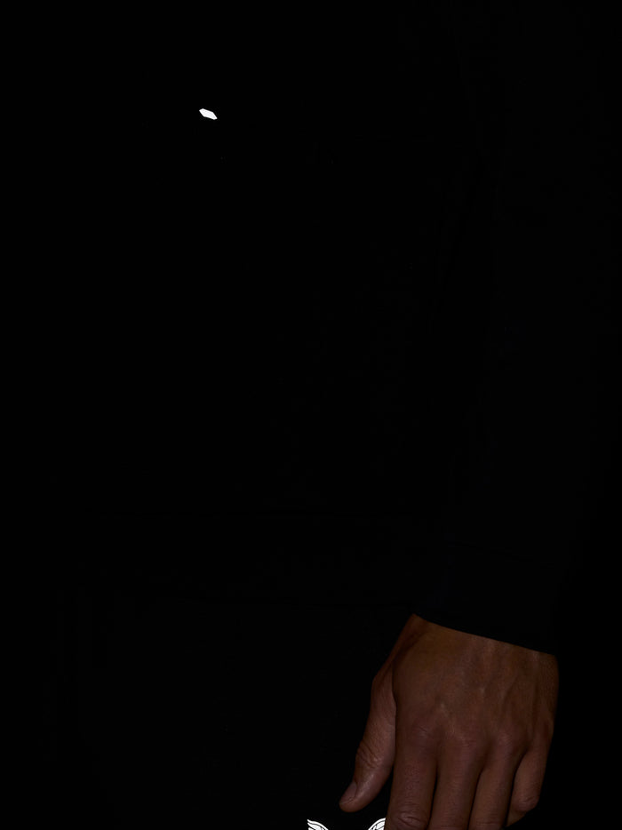 Close up of black Castore Travel Lifestyle Sweatshirt showing white wing logo on chest with a hand resting by the sleeve
