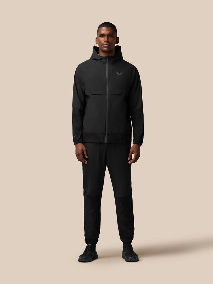 Full-body view of a model wearing the black Flex Winterised Woven Jacket with hood and matching pants.
