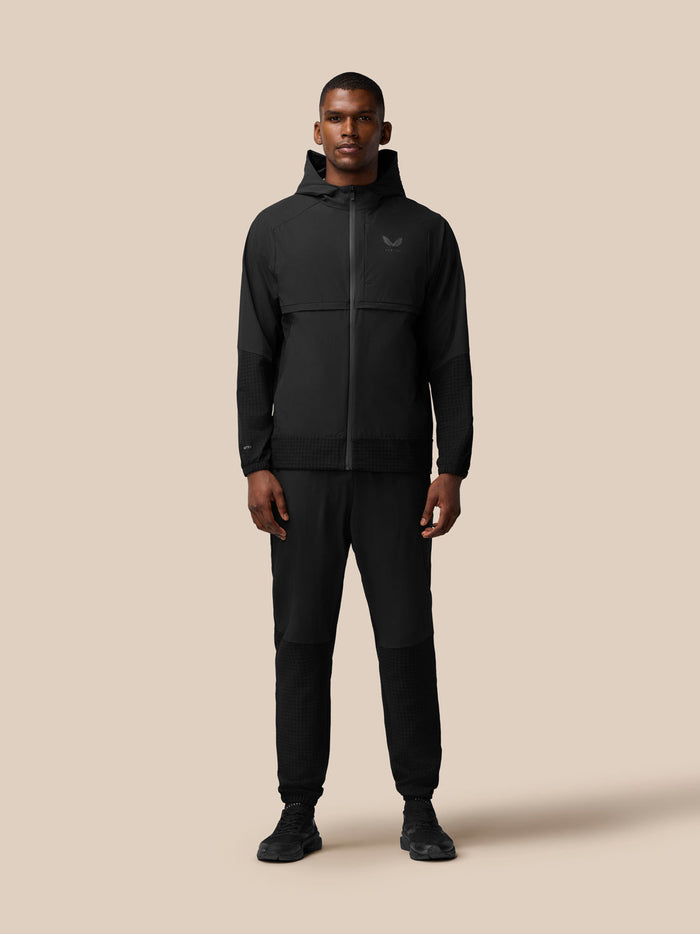 Full-body view of a model wearing the black Flex Winterised Woven Jacket with hood and matching pants.