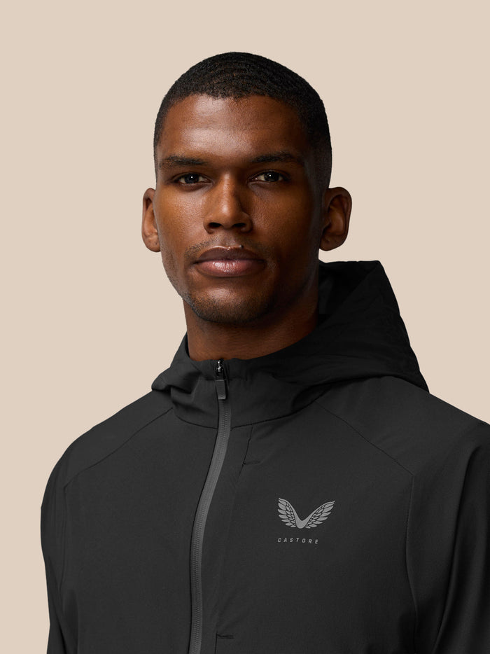 Close-up of a model wearing the black hooded Flex Winterised Woven Jacket with a chest logo.