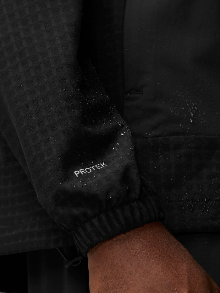 Close-up of black Flex Winterised Woven Jacket sleeve with ProTek branding and water droplets.