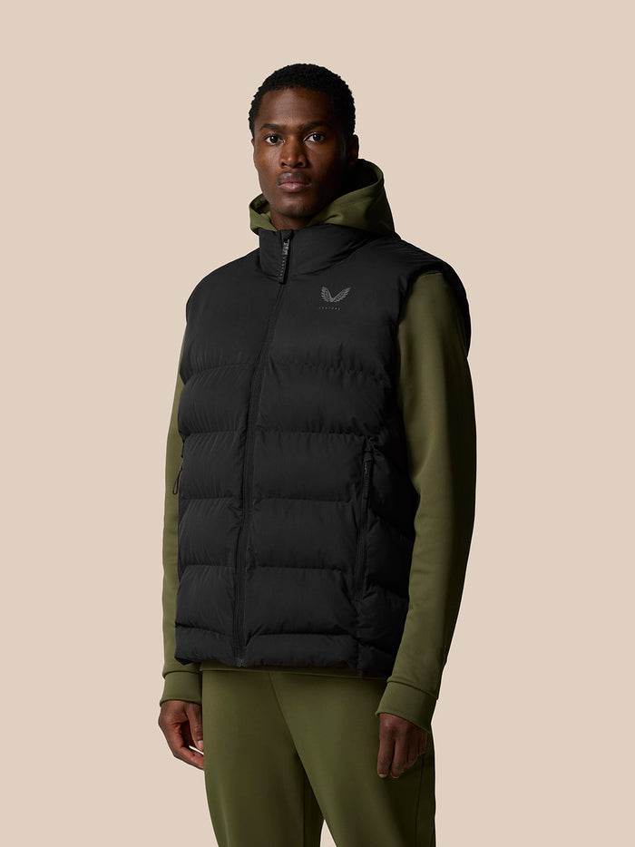 Full body front view of a man in a black puffer gilet with an olive green hoodie and matching olive pants