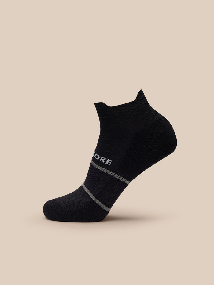 Close up of black training sock with Castore branding and gray stripes against a beige background