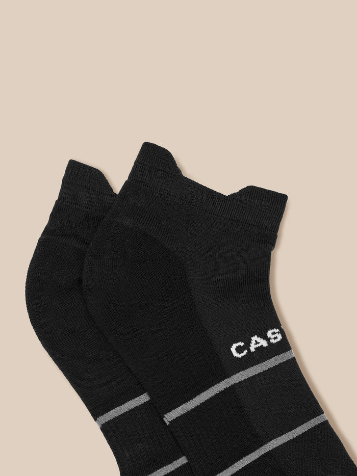Three black active training socks with grey stripes and Castore branding against a beige background