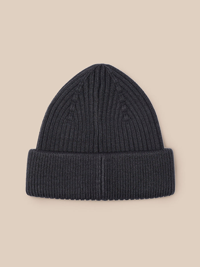 Close-up of dark grey ribbed knit beanie showing Castore logo patch on the folded cuff.